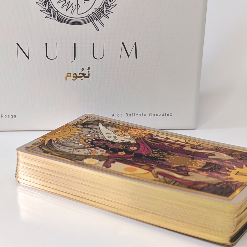 NUJUM board game box with a detailed illustrated deck of gold-edged cards in the foreground, showcasing mystical artwork and premium finish